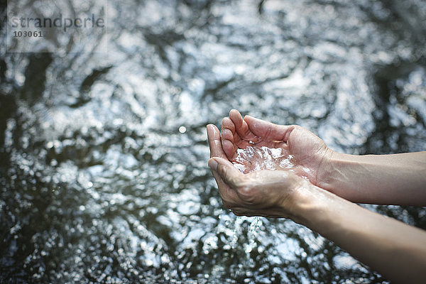 Ein Mann  der seine Hände schröpft und klares Wasser aus einem Fluss schöpft.
