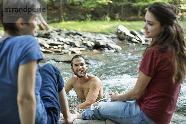 Ein Mann im Fluss und zwei Frauen am Flussufer sitzend.