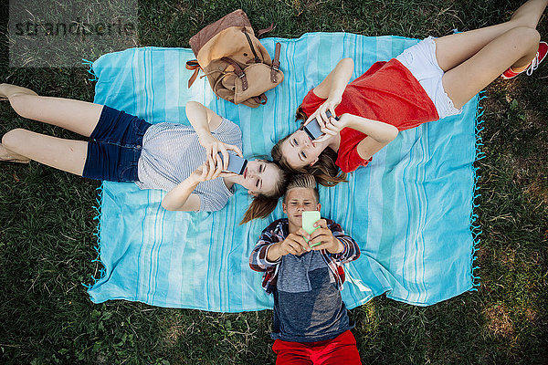 Drei Teenager-Freunde mit Smartphones auf der Decke liegend