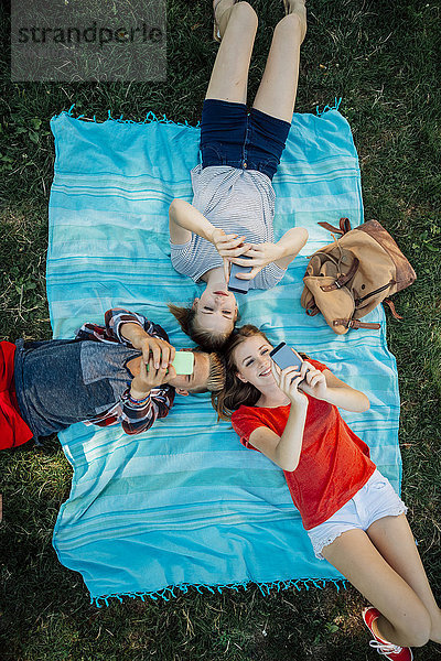 Drei Teenager-Freunde mit Smartphones auf der Decke liegend