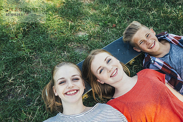 Drei glückliche Teenager-Freunde liegen auf dem Skateboard auf der Wiese.