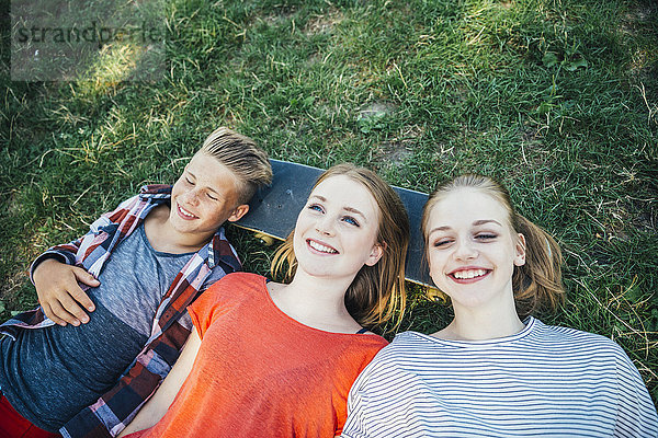 Drei glückliche Teenager-Freunde liegen auf dem Skateboard auf der Wiese.