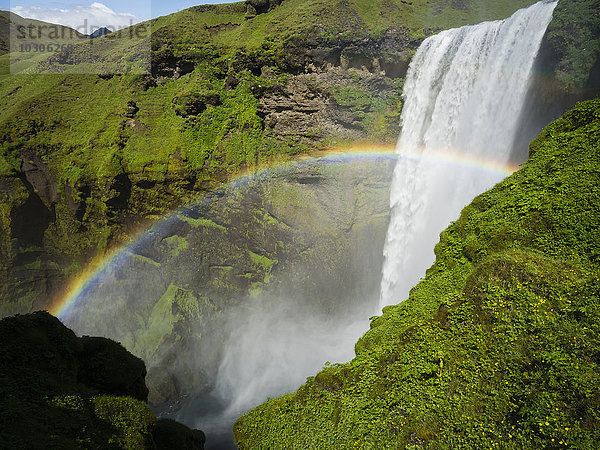 Wasserfall Skogafoss  eine Kaskade über einer steilen Klippe und ein Regenbogen im Nebel.