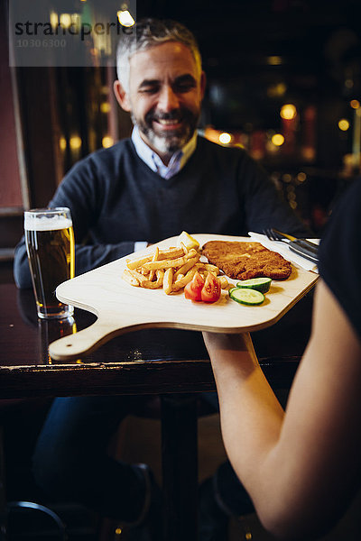 Lächelnder Mann im Restaurant empfängt Wiener Schnitzel mit Pommes frites
