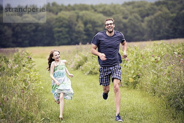 Ein Mann und ein kleines Kind rennen durch eine Wildblumenwiese.