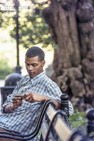 Ein Mann  der mit seinem Smartphone auf einer Parkbank sitzt