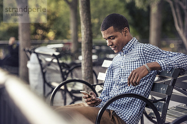 Ein Mann in einem Park  der ein Smartphone ansieht