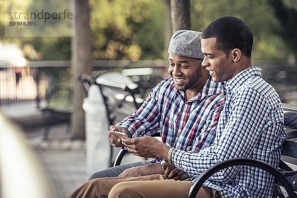 Zwei Männer sitzen in einem Park und schauen auf ein Smartphone