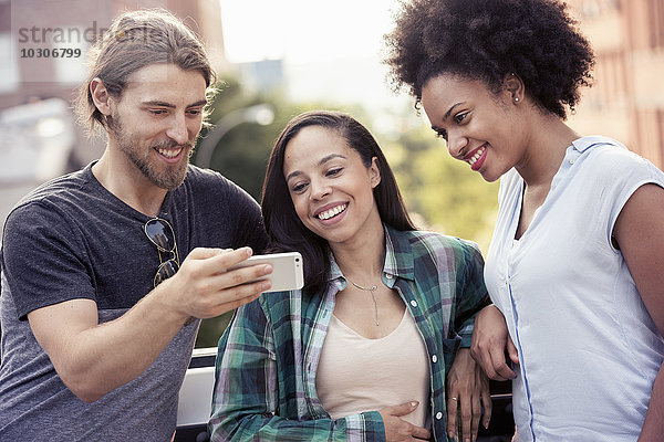 Ein Mann und zwei Frauen schauen auf ein Smartphone