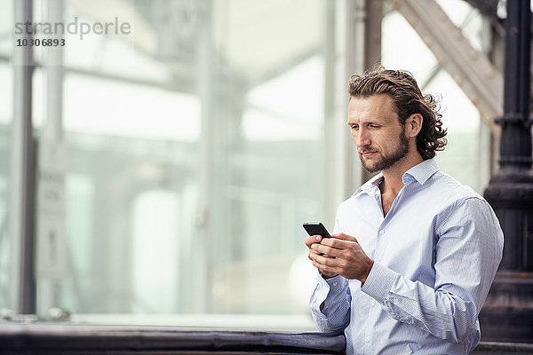 Ein Mann steht draußen auf der Straße und überprüft sein Mobiltelefon.