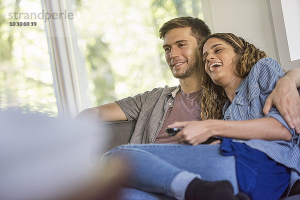 Ein Paar  ein Mann und eine Frau sitzen lachend nebeneinander und schauen auf einen Bildschirm.
