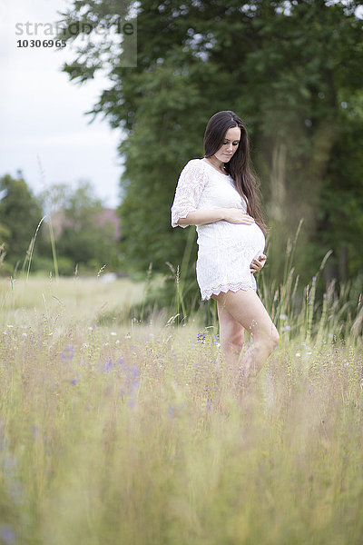 Schwangere Frau  die auf einer Wiese steht und ihren Bauch hält.