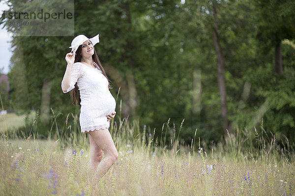 Porträt einer schwangeren Frau in weißer Kleidung auf einer Wiese stehend