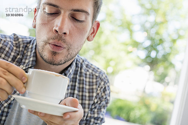 Ein Mann bläst auf die Oberfläche seines heißen Kaffees.