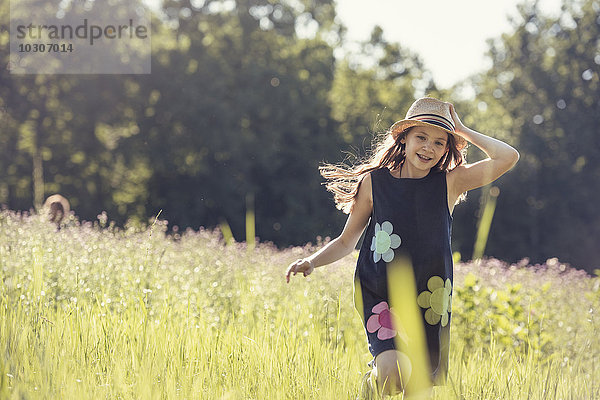 Ein Kind  ein junges Mädchen mit Strohhut auf einer Wiese mit Wildblumen im Sommer.