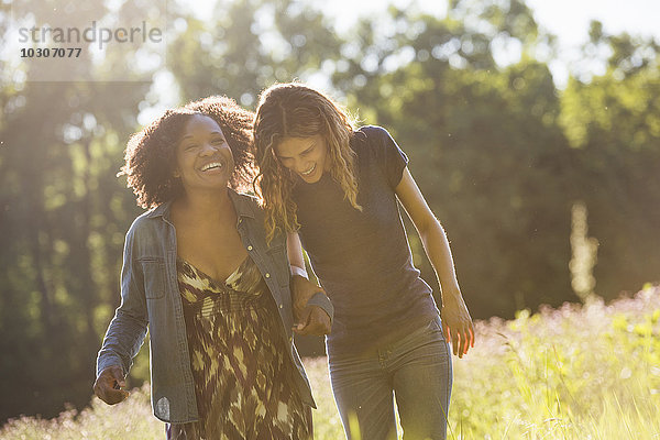 Zwei Frauen gehen durch ein Feld  unterhalten sich und lachen.