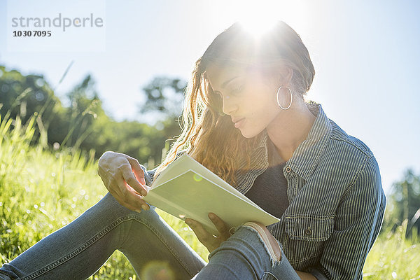Eine junge Frau sitzt in der Sonne und liest ein Buch