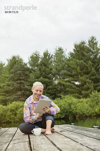 Eine Frau sitzt im Freien auf einem Steg und benutzt ein digitales Tablett.