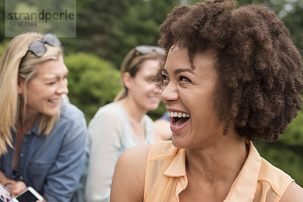 Eine Frau in einer Gruppe von Freunden im Freien beim Lachen.