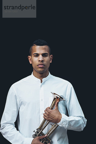 Porträt eines jungen Mannes mit Trompete vor schwarzem Hintergrund