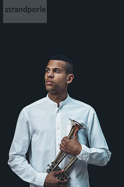Porträt eines jungen Mannes mit Trompete vor schwarzem Hintergrund