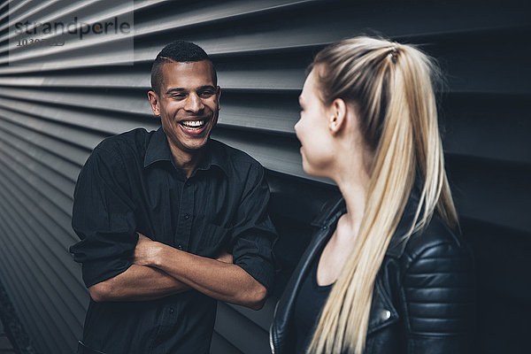 Schwarz gekleideter junger Mann von Angesicht zu Angesicht mit junger Frau vor schwarzer Fassade