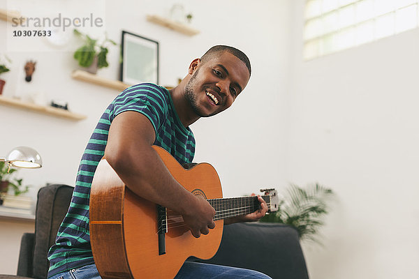 Porträt eines lächelnden Mannes  der zu Hause Gitarre spielt.