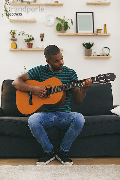 Mann sitzt auf einer Couch und spielt Gitarre.