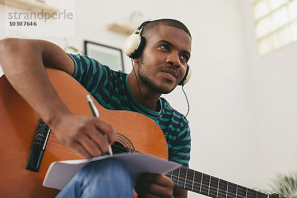 Mann mit Gitarre hört Musik mit Kopfhörern  die etwas aufschreiben.