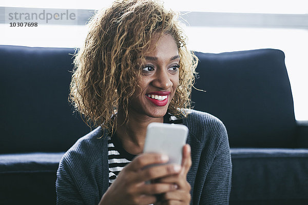 Porträt einer lächelnden jungen Frau mit ihrem Smartphone