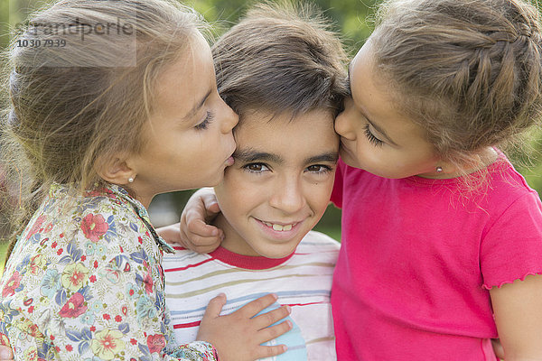 Zwei kleine Mädchen  die einen Jungen küssen.