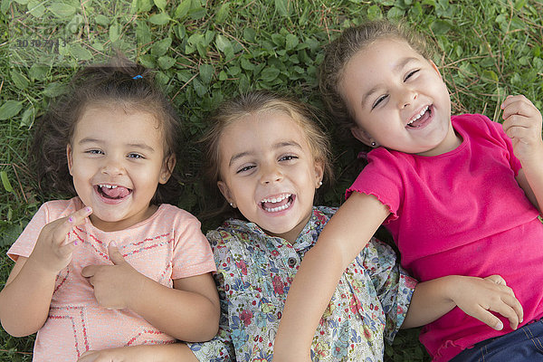 Porträt von drei lachenden kleinen Mädchen  die nebeneinander auf einer Wiese liegen.