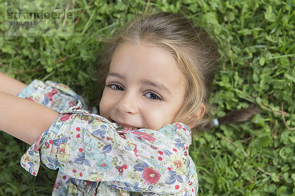 Porträt eines lächelnden kleinen Mädchens auf einer Wiese liegend