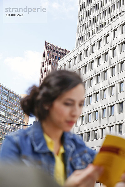 Deutschland  Berlin  junge Frau beim Lesen vor der Fassade am Potsdamer Platz