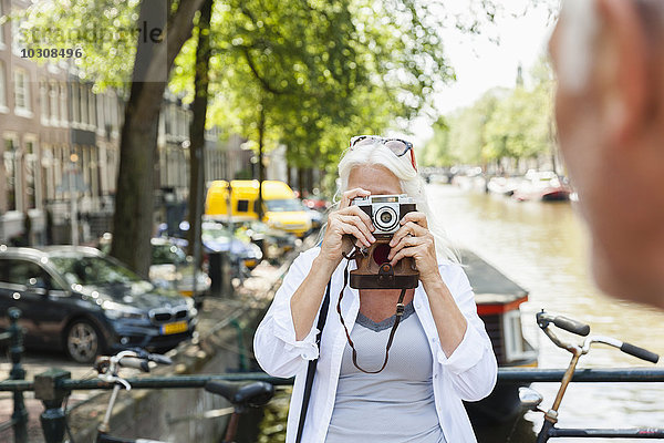 Niederlande  Amsterdam  Seniorin beim Fotografieren mit Analogkamera am Stadtkanal