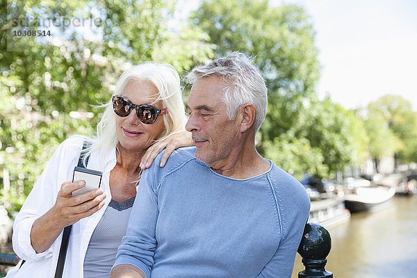 Niederlande  Amsterdam  Seniorenpaar mit Handy am Stadtkanal