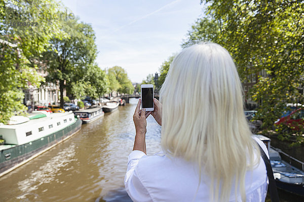 Niederlande  Amsterdam  Seniorenfrau macht Handyfoto am Stadtkanal