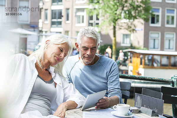 Niederlande  Amsterdam  Seniorenpaar mit digitalem Tablett in einem Outdoor-Café