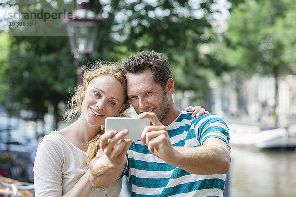 Niederlande  Amsterdam  lächelndes Paar  das einen Selfie am Stadtkanal nimmt.