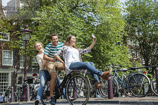 Niederlande  Amsterdam  drei verspielte Freunde auf einem Fahrrad in der Stadt