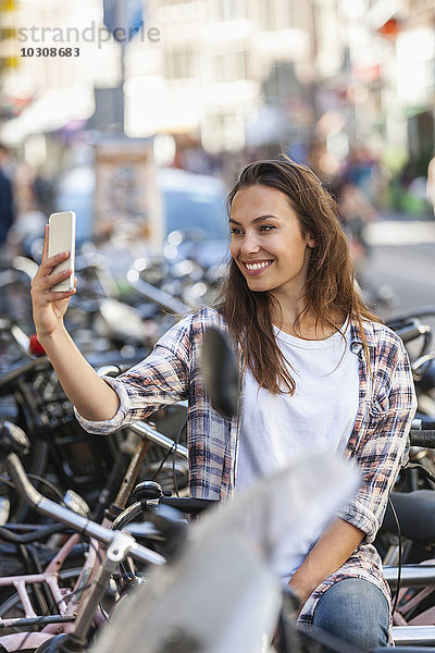 Niederlande  Amsterdam  lächelnde junge Frau mit einem Selfie