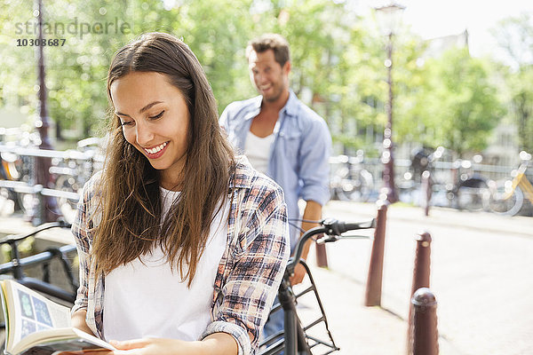 Niederlande  Amsterdam  lächelnde junge Frau liest Buch mit Mann im Hintergrund