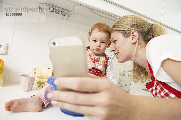 Junge Frau  die einen Selfie mit ihrer kleinen Tochter in die Küche nimmt