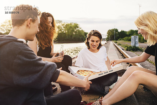 Freunde sitzen zusammen im Freien und teilen sich eine Pizza.