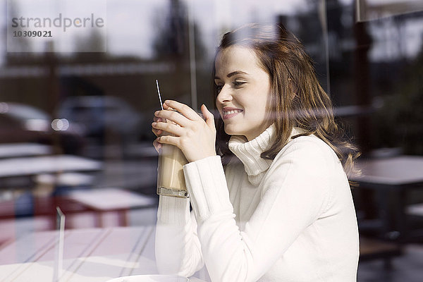Lächelnde junge Frau mit Latte Macchiato sitzend in einem Cafe und schauend