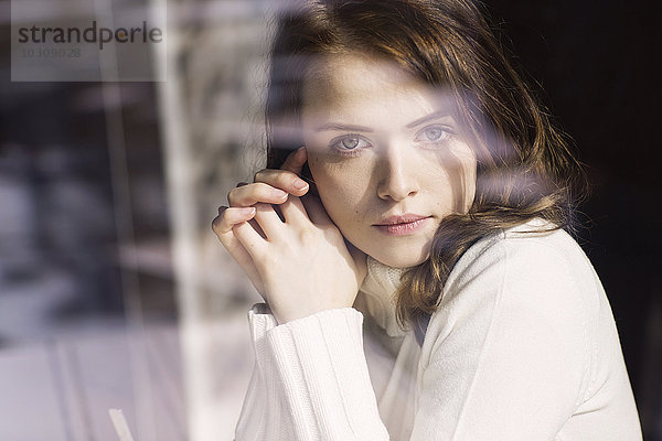 Porträt einer jungen Frau  die durch die Fensterscheibe eines Cafés schaut.