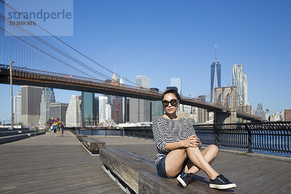USA  New York City  Porträt einer jungen Frau auf einer Bank vor der Brooklyn Bridge