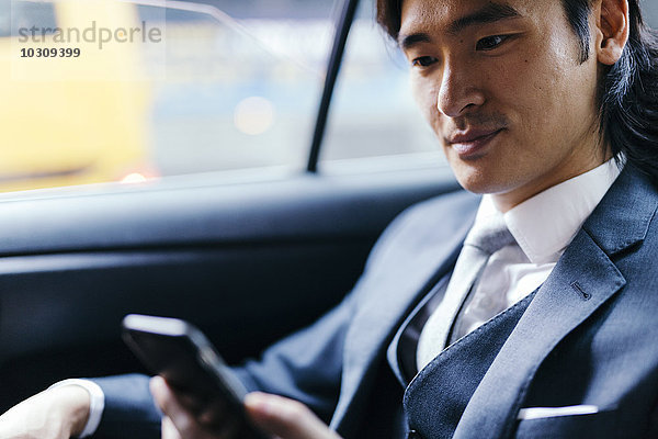 Lächelnder Geschäftsmann auf dem Rücksitz des Autos per Handy