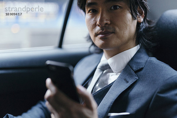 Portrait eines Geschäftsmannes auf dem Rücksitz eines Autos mit Handy