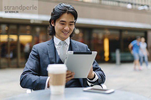 USA  New York City  lächelnder Geschäftsmann im Outdoor-Café mit Blick auf digitales Tablett